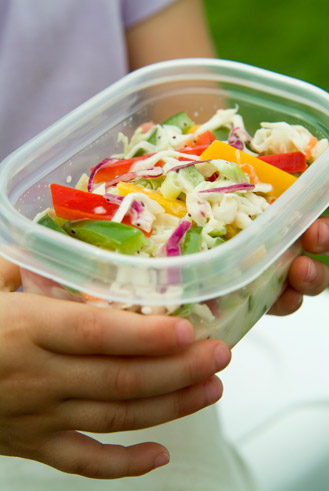 close up of young girls hands holding a container of brightly colored salad