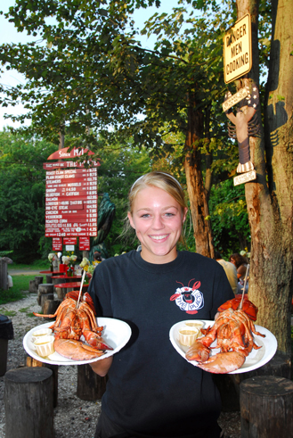 young woman holding two plates of lobsters at an outdoor eatery