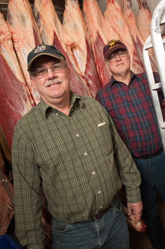two men standing in front of hanging beef